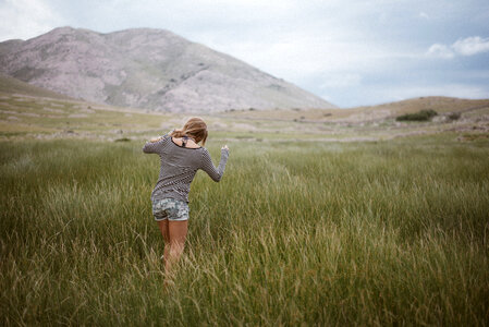 Young Girl Wearing Striped Shirt Walking Through A Green Meadow photo