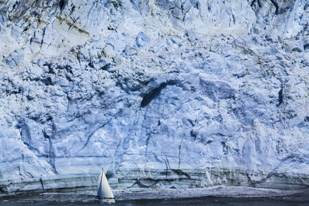 Small Sailboat against a Huge Blue Iceberg photo