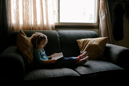 Young Girl Reading a Book and Sitting on Sofa at Home photo