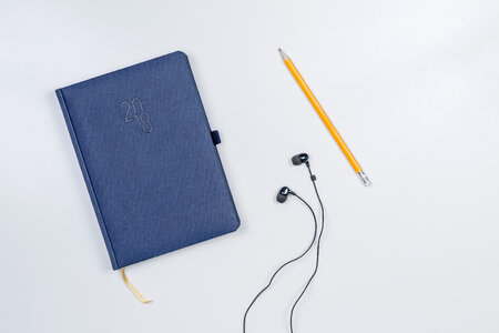 Pretty diary with a pencil and headphones on the white table. photo