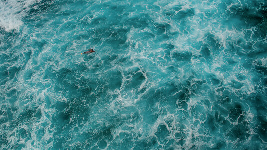 Aerial View of a Man on a Surfboard in the Turquoise Ocean photo