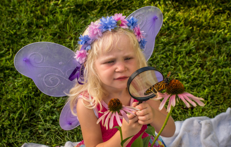 Little girl looks at monarch through eye glass