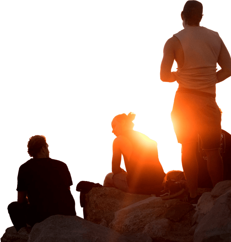 Two Men Sitting And One Man Standing Near Cliff Taken During Golden Hour