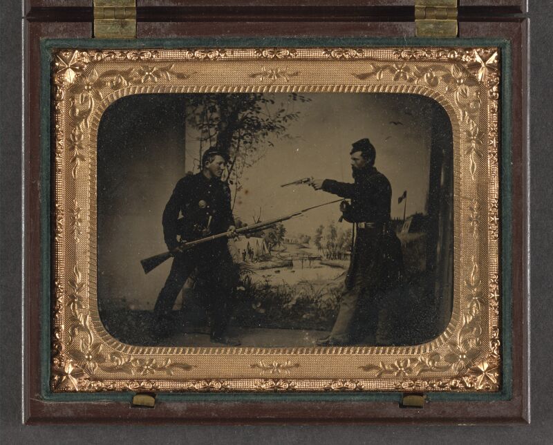 Two unidentified soldiers in Union uniforms posing with bayoneted Springfield Model 1861 rifled musket with attached bayonet, knife, and Colt Model 1851 Navy revolver in front of painted LCCN2010650759, between 1861 and 1865