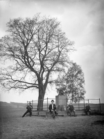 Monument to Captain Hirsch with seated gentlemen and children on the base of the enclosure, next to a locust tree and birch trees, Ermenegildo Antonio Donadini, um 1900