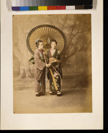 Two Japanese women, full-length studio portrait with backdrop, facing slightly right, standing with large parasol and holding hands LCCN2009632869, 1877