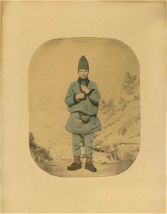 53. Mannsdrakt, samedrakt, Salten. Portrett av mann stående i fotoatelier foran malt naturbakgrunn - Norsk folkemuseum - NF.07785-002 (1)