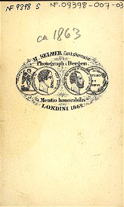53. Mannsdrakt, samedrakt, Salten. Portrett av mann stående i fotoatelier foran malt naturbakgrunn - Norsk folkemuseum - NF.09398-007 (2)