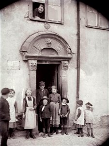 En samling barn framför en port och en kvinna som tittar fram i ett fönster ovanför, Stockholm - Nordiska Museet - NMA.0052524