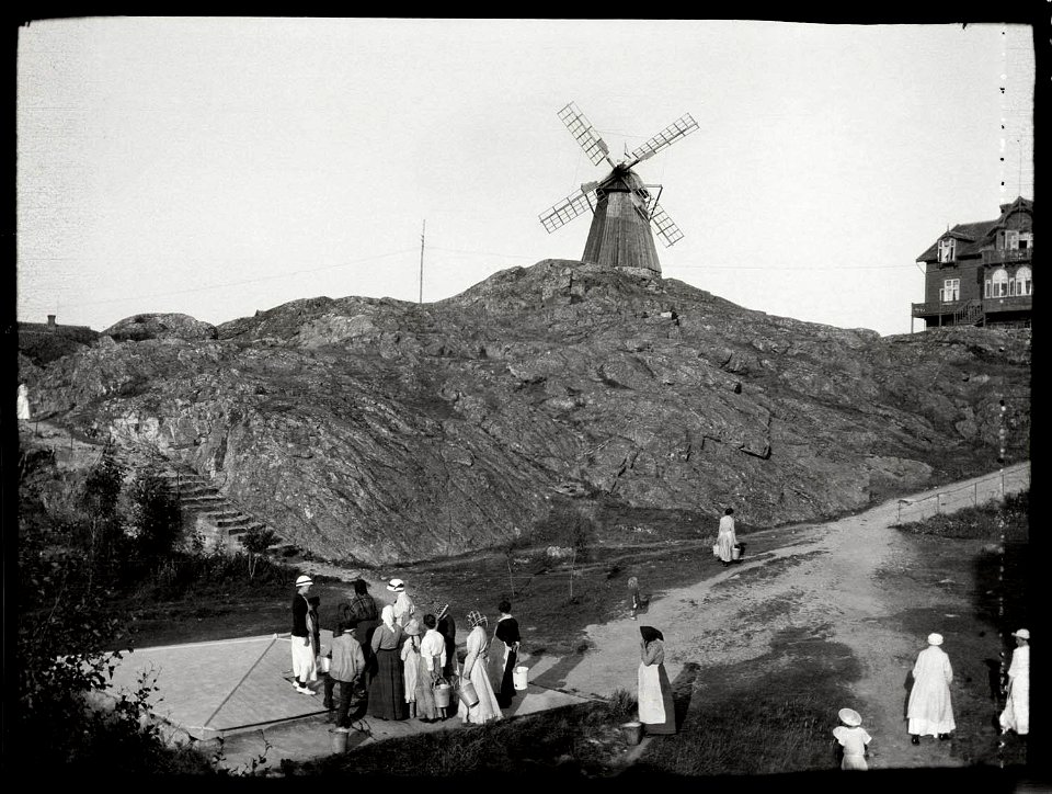 Fiskebäckskil, brunn. Människor samlade vid en brunn, i bakgrunden väderkvarn - Nordiska Museet - NMA.0044914