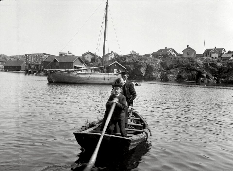 Pojke med åra och två personer stående i liten båt - Nordiska Museet - NMA.0054394
