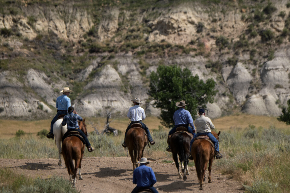 A group of young people horseback riding in the grassy field
