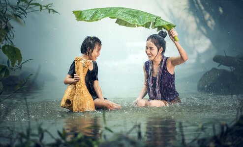 Two girls hiding from the rain under a large leaf plants