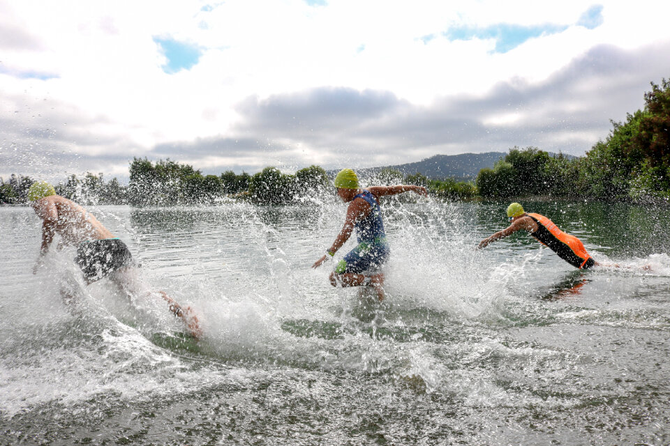 Three triathlon participants running into the water for swim