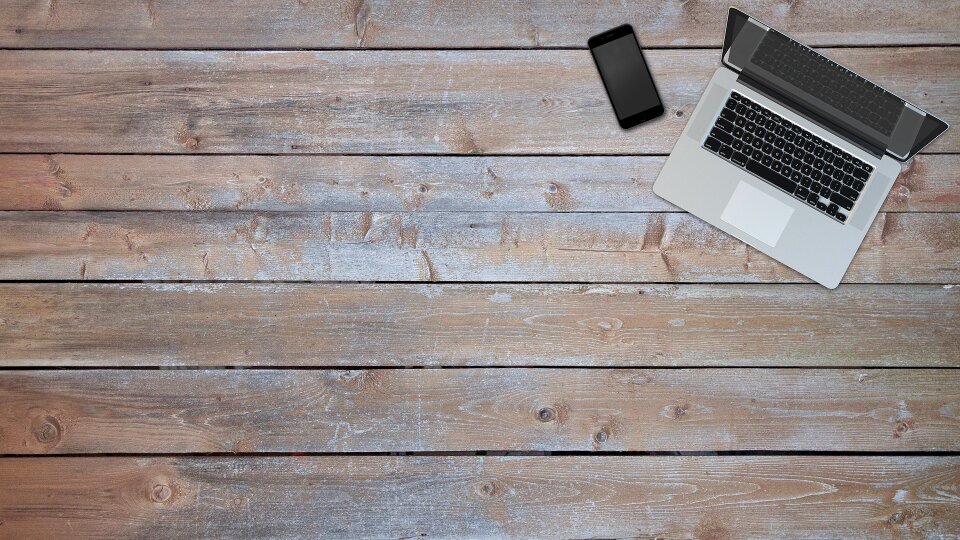 laptop with blank screen on wooden table next to gray wall