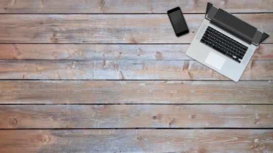 laptop with blank screen on wooden table next to gray wall