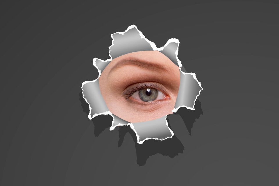 Womans eye peeking through a hole in white paper