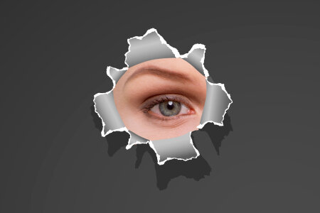 Womans eye peeking through a hole in white paper photo