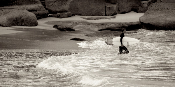 surfer with surfboard walks along the beach in the day time