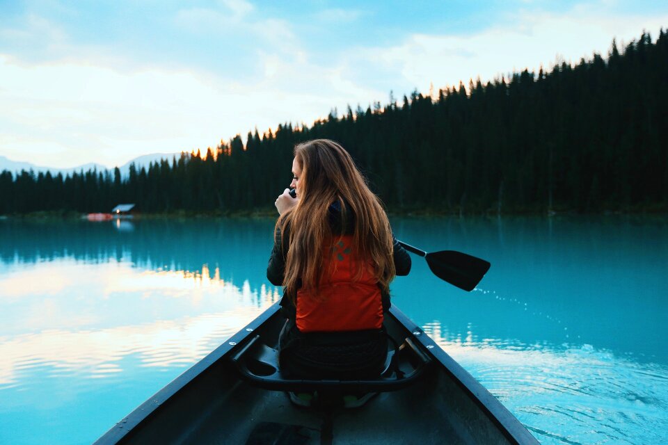 Girl with paddle and kayak on a small river in rural landscape