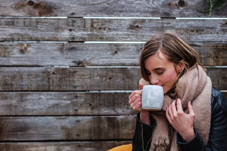 Blonde woman in a blanket scarf and jacket sipping coffee photo