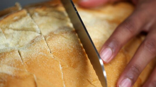 Close up of a someone slicing fresh bread with sharp knife. photo