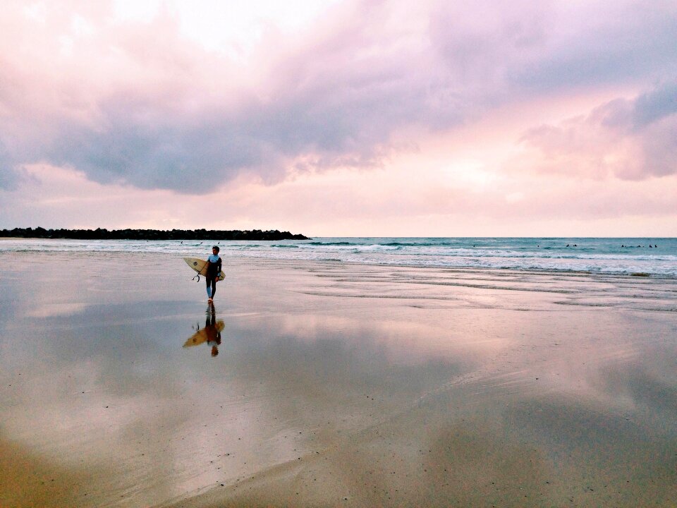 A man is walking with a surf in his hands across the sea shore