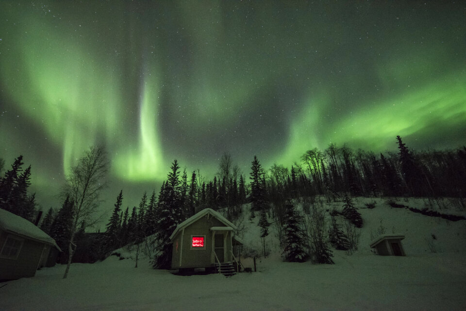 Aurora dances and shimmers overhead above a cabin at Coal Creek