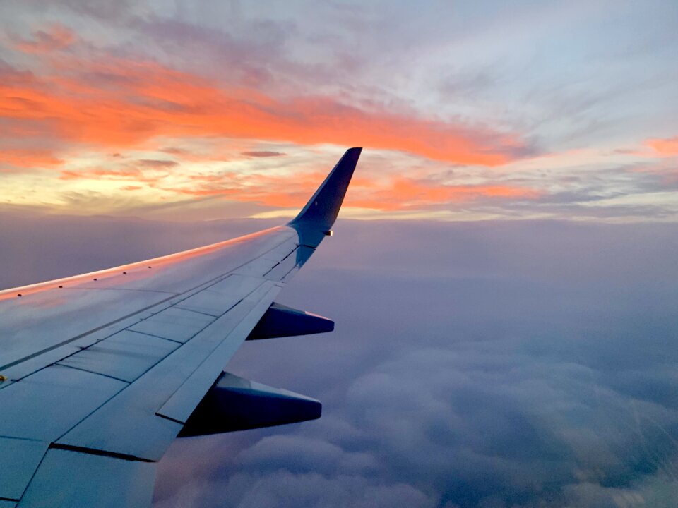 Wing of airplane reflecting sunset over the clouds