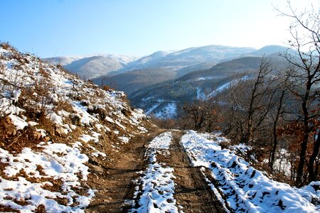 Rural unpaved road waving over the hills and mountains on a snowy photo