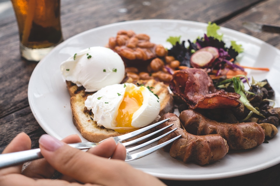 Eating high protein brunch with poached eggs, beans and bacon