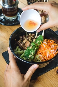 Girl pouring hot sauce on her Vietnamese food