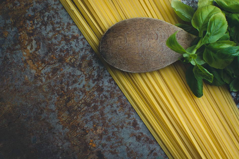 Pasta spaghetti with basil and wooden spoon on a rusty metallic background