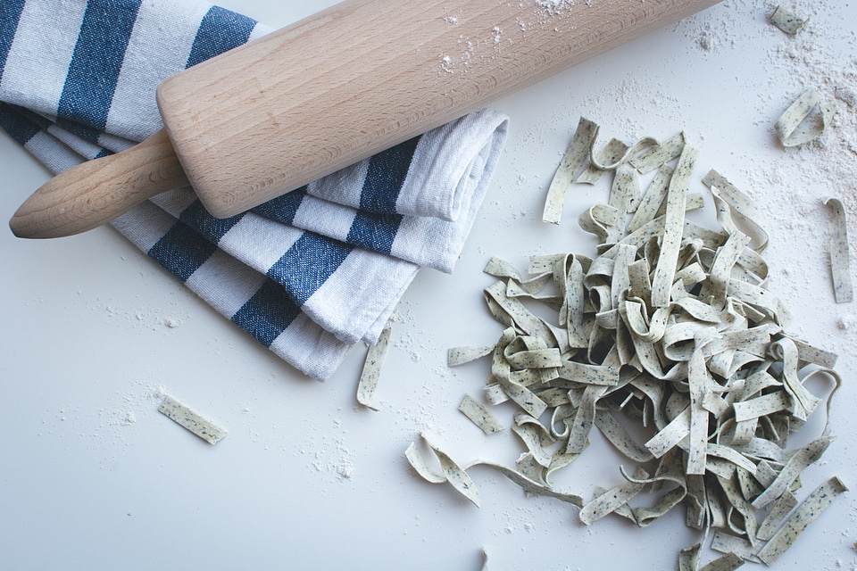 Pasta tagliatelle covered by flour with a wooden roller on a white background