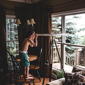 A Young Boy Observing the Nature Through a Telescope from Indoors photo
