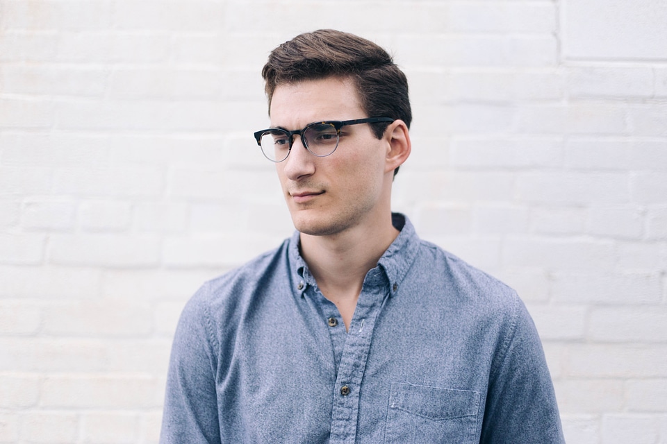 Man Wearing Glasses in Front of White Brick Wall