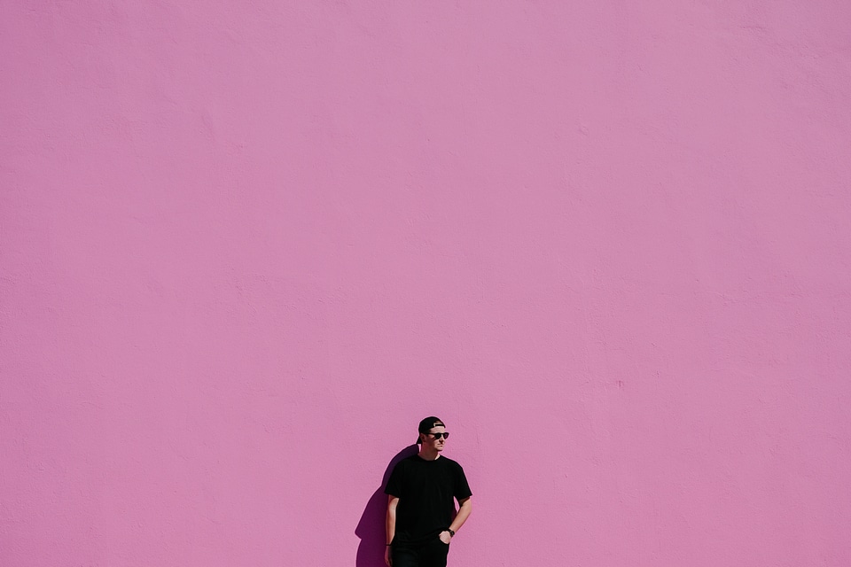 Man in Black T-shirt, Cap andSunglasses Leaning on Pink Wall