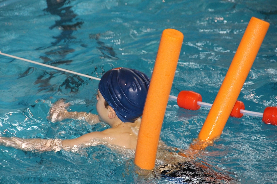 Funny little boy swims in a pool in an orange life preserver