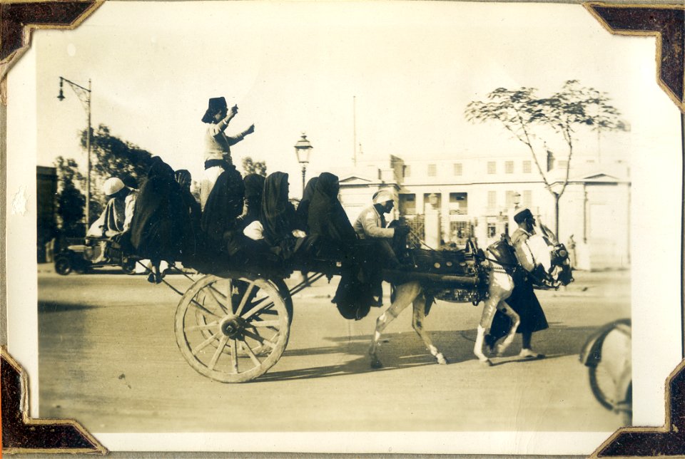 Egyptian ladies seated in a wagon, accompanied by four men.