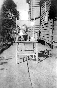 Baby seated in chair outside a house, [n.d.] photo