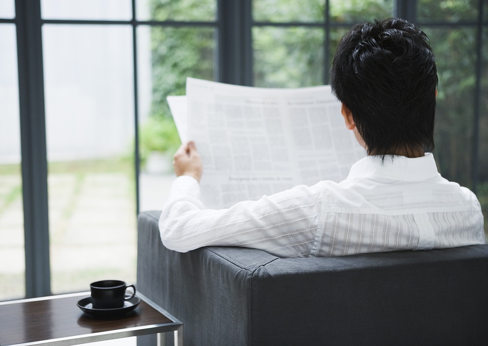 Man sitting on couch at home reading reading newspaper .