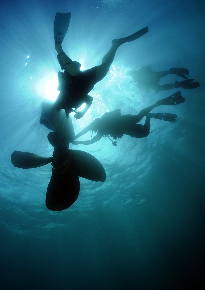Scuba divers in silhouette swimming under water