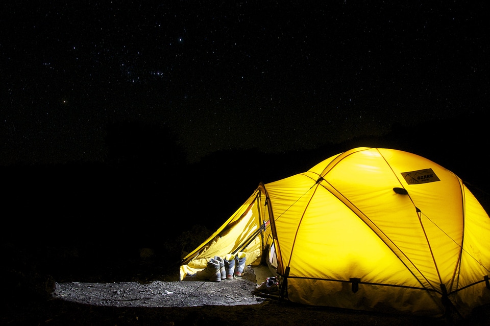 A camping tent glows under a night sky full of stars