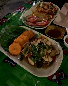 This is a mix of traditional thai foods and western kitchen. Thai Chicken with fish souse, salad, carrots and cashew nuts. With a side order of chicken wings, chips with cucumber and tomato. Served in a traditional thai street restaurant. photo