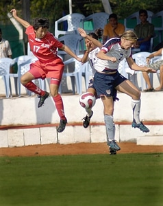 Girls heading soccer ball during match against blue sky photo