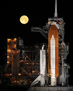 A nearly full moon sets as the space shuttle Discovery