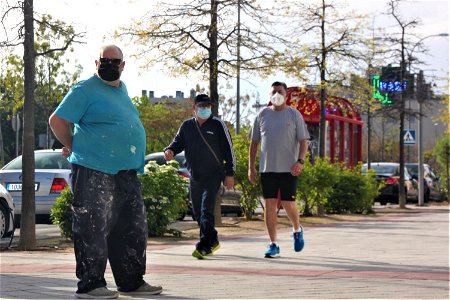 Pintor parado en la calle y dos hombres paseando con mascarillas