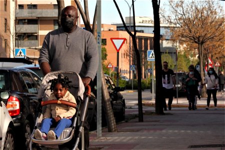 Hombre negro con una mascarilla lleva un carrito y una niña pequeña en él photo