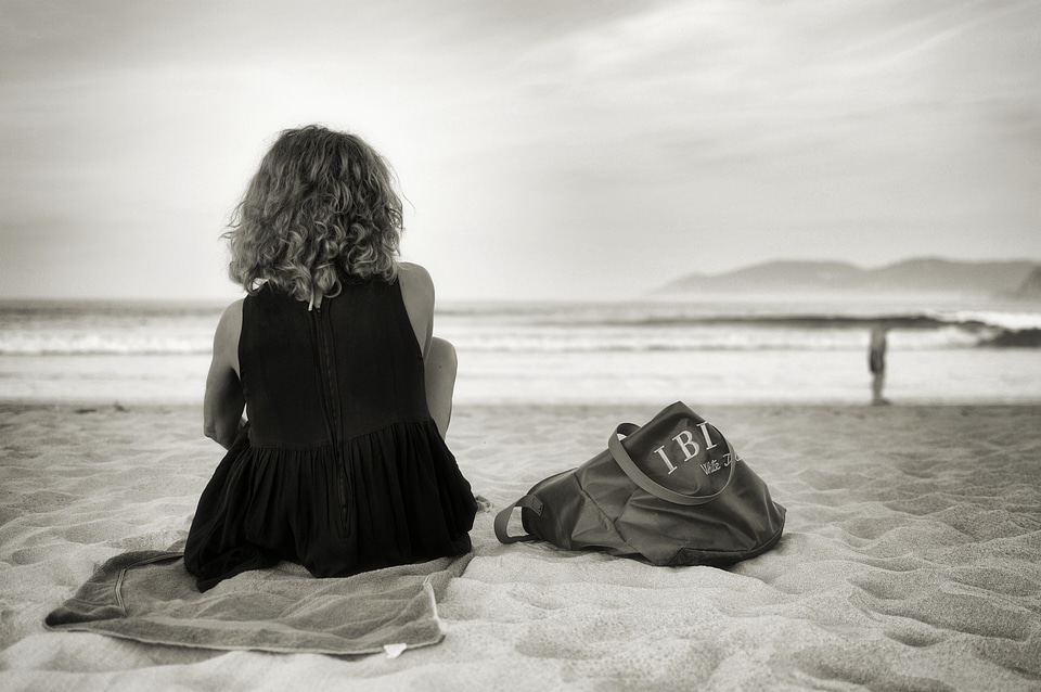 A young slim woman seated on a black sand beach