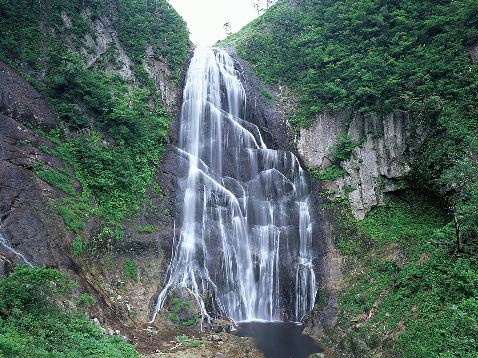 Alpine waterfall in mountain forest under sky.